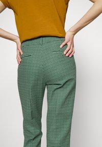 Groene broek met een ruitpatroon. Bevat twee achterzakken en heeft een slim-fit snit, gecombineerd met een mosterdkleurig top. Gladde textuur.