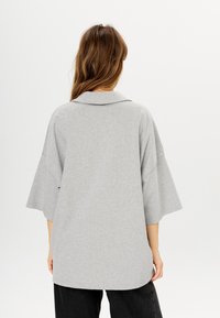 Grauer, übergroßer Pullover mit weitem Kragen und kurzen Ärmeln. Weiche Textur und verlängerte Rückenpartie. Keine sichtbaren Muster oder Hardware-Akzente.