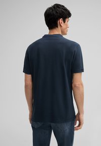 Polo bleu marine en coton, avec col, manches courtes et ourlet droit. Le dos présente une texture lisse avec des coutures minimales.