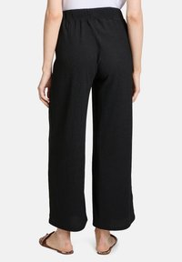 Zwarte wijde broek gemaakt van gestructureerde stof. Heeft een elastische tailleband en een losse pasvorm, met een soepele afwerking bij de boorden.