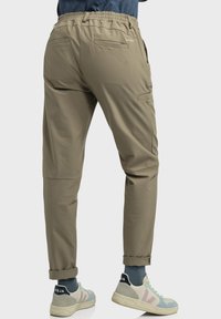 Leichte, khakifarbene Hose mit elastischem Bund, zwei Gesäßtaschen, schmal zulaufenden Beinen und aufgerollten Säumen, kombiniert mit mehrfarbigen Sneakers.