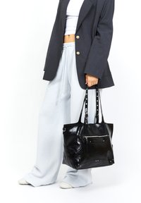 Borsa a tracolla nera in pelle con texture lucida, tasca frontale con zip e dettagli borchiati. Ha doppi manici e un design spazioso.