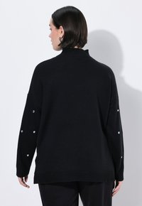 Maglione nero a maglia con colletto alto, vestibilità ampia e maniche lunghe, caratterizzato da strass decorativi sulle maniche. Design semplice sul retro.