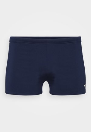 Námornícke modré plavky vyrobené z elastického materiálu, s priliehavým strihom a elastickým pásom. Obsahujú malé biele logo na dolnej strane.