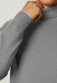 Grå turtlenecktröja i mjukt, finstickat material. Har ribbade mudd och krage, vilket ger en slät, enhetlig textur.