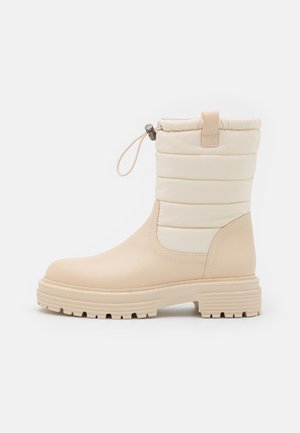 Beige wasserdichte Stiefel mit gestepptem elfenbeinfarbenem Obermaterial, runder Zehenpartie und strukturiertem Gummilaufsohle. Mit einem Zugverschluss an der Oberseite.