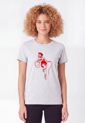 Femme aux cheveux bouclés portant un t-shirt gris clair avec un dessin rouge d'une cowgirl dansante tenant un lasso.