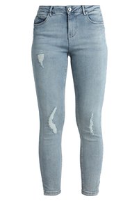 Jeans skinny de denim azul claro con detalles desgastados y parches deshilachados. Presenta un diseño clásico de cinco bolsillos y cierre con botón de metal.
