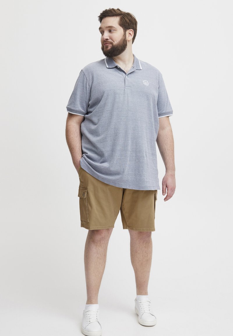Grå polo skjorte med hvite krageakenter, parret med beige cargo shorts og hvite joggesko. Stoffet ser jevnt ut med en subtil tekstur.