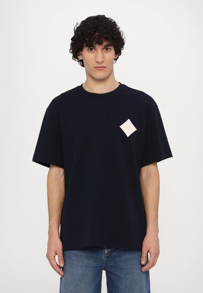 Marineblå bomulds T-shirt med afslappet pasform, korte ærmer og en crèmefarvet diamantpatch på brystet.