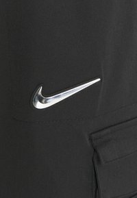 Czarne materiałowe spodnie z srebrnym logo Swoosh Nike po lewej stronie oraz dodatkowymi kieszeniami na nodze.