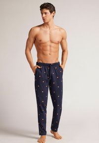 Marinblå pyjamasbyxor med elastisk midja, prydda med ett heltryckt orange diamantmönster, två sidofickor och en avslappnad passform.