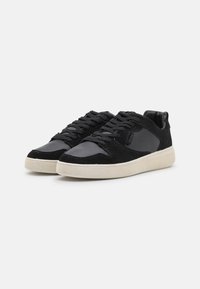 Black sneakers with suede and leather panels, featuring a textured surface, flat laces, and a light-colored rubber sole.