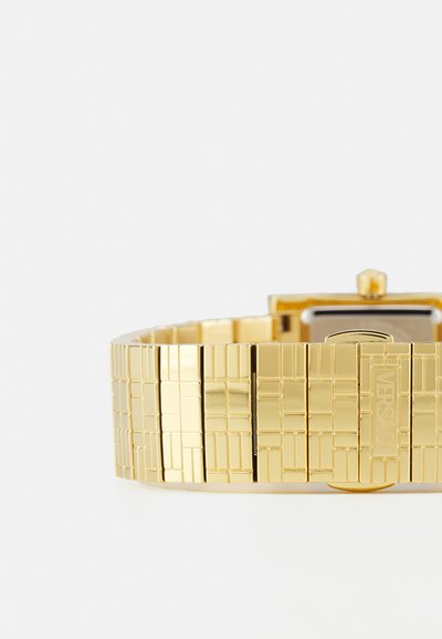 Gold metal wristwatch with a textured rectangular link bracelet, square face, and engraved branding detail. Features a polished finish.