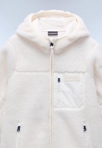 Witte fleecjas met capuchon, voorzien van een gestructureerd oppervlak, ritszakken en contrasterende paneeldetails in een glad, licht materiaal.