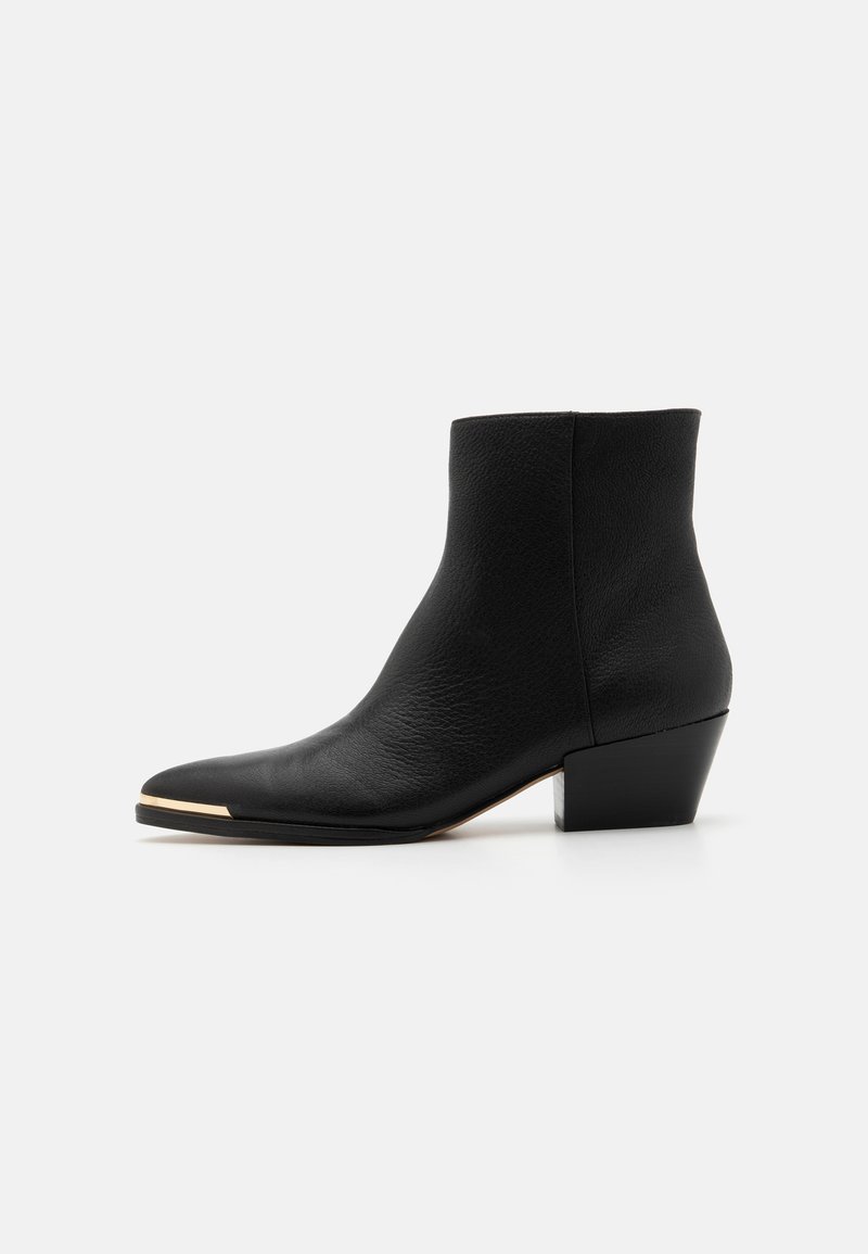 Botín de cuero negro hasta el tobillo con punta afilada, tacón bajo y un acento dorado en la punta. Superficie texturizada con un diseño limpio y minimalista.