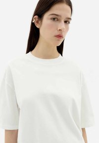 Weißes Baumwoll-T-Shirt mit rundem Halsausschnitt, kurzen Ärmeln und lockerer Passform. Glatte Textur, minimalistisches Design und keine sichtbaren Verzierungen.