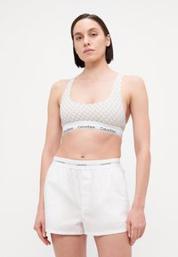 Calvin Klein sportmelltartó világos bézs színben, geometrikus mintával, fehér pamut rövidnadrággal párosítva, mely rugalmas derékpánttal és logóval rendelkezik.