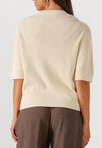 Crème ribgebreid T-shirt met korte mouwen en een ronde halslijn, gecombineerd met een bruine broek. Gelaagde stof en een relaxte pasvorm.
