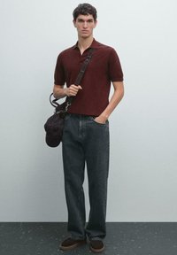Bordeaux polo-shirt, mørk denim bukser, brune ruskind sko, bærer en mørk taske. Simpel design, korte ærmer, afslappet pasform. Glat tekstur.
