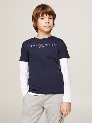 Navy Baumwoll-T-Shirt mit dem Logo "TOMMY HILFIGER EST. 1985", darüber ein weißes Langarmhemd, kombiniert mit grauen Sweatpants.