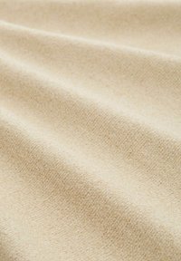 Beige textil med struktur och en subtil väv, som visar mjuka veck som skapar skuggor och ljusreflexer över ytan.