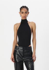 Czarny body z wysokim kołnierzem wykonane z gładkiego materiału, z wycięciami po bokach, zestawione z czarnymi spodniami z wysokim stanem z ekologicznej skóry.