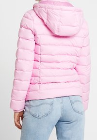 Rosa Puffjacke mit Kapuze, die horizontale gesteppten Abschnitte und elastische Bündchen aufweist, kombiniert mit hellblauen Denim-Jeans.