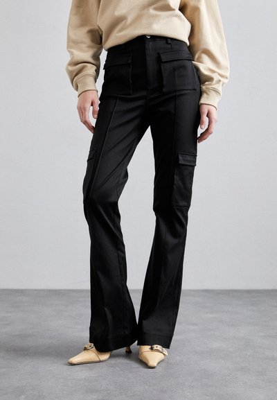 Pantaloni cargo negri cu talie înaltă, având buzunare laterale și un design cu picior drept, asortați cu pantofi ascuțiți de culoare deschisă.