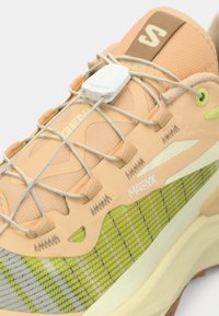 Μπεζ και πράσινο αθλητικό παπούτσι με μπεζ κορδόνια, λευκό κλείδωμα κορδονιών, το κείμενο "MATRIX" στην πλευρά και υφή στην σόλα, απεικονιζόμενο σε κοντινή γωνία.