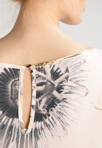 Vue arrière d'un blouse avec un décolleté large et une ouverture en forme de serrure, ornée d'un motif floral dans des couleurs atténuées sur un fond en tissu clair.