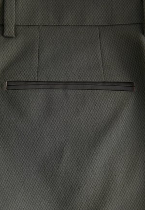 Graue Stoffhosen mit einem strukturierten Muster. Sie haben einen geraden Schnitt und eine Leistentasche auf der Rückseite, die mit schwarzem Stoff besetzt ist.