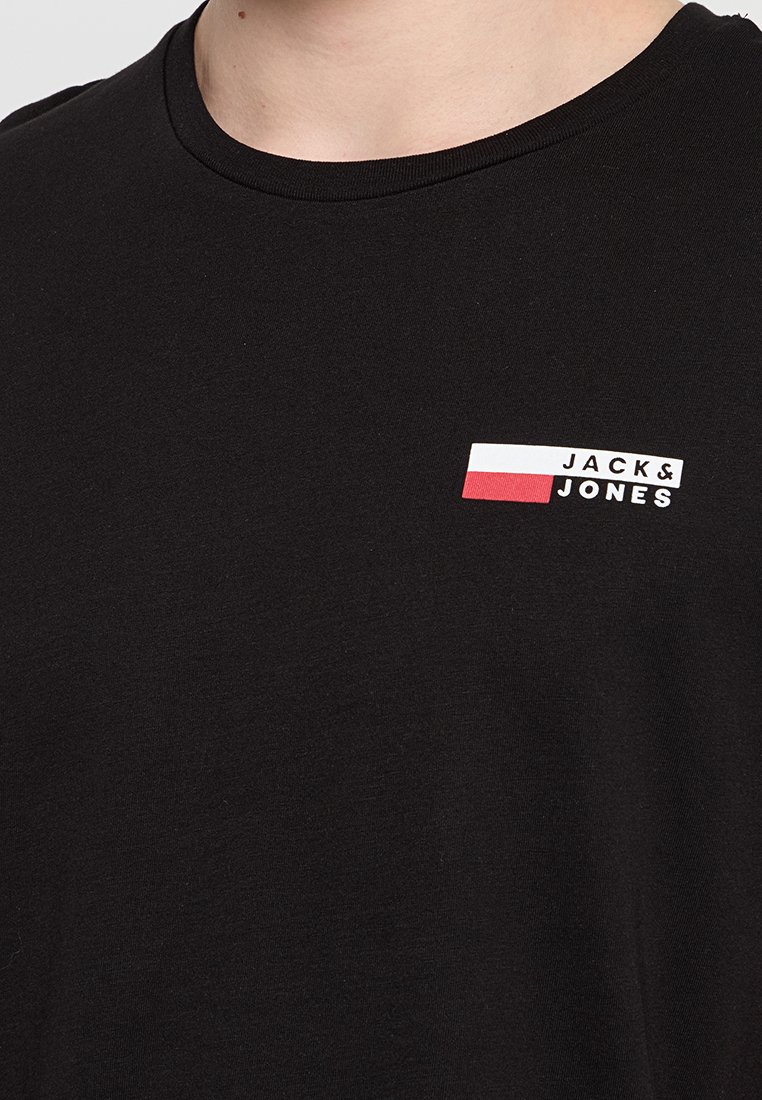 Schwarzes Baumwoll-T-Shirt mit rundem Halsausschnitt und einem Logo-Patch in Weiß, Rot und Blau auf der linken Brust. Weicher Stoff.