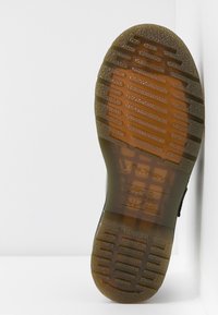 Semelle de chaussure en caoutchouc noir avec un motif de grip texturé, comprenant des rainures et une étiquette en relief pour la résistance au glissement et à l'huile.