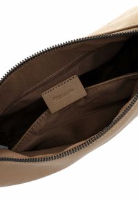 Interno di una borsa a tracolla in pelle marrone con una cerniera, più scomparti, texture liscia e un'etichetta con la scritta "Tamaris" in rilievo.