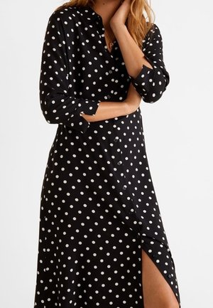Czarna midi sukienka z guzikami w białe kropki, z rękawami do połowy przedramienia i rozcięciem na wysokości uda po prawej stronie.