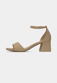 Sandale ouverte beige avec un large talon bloc, sangle de cheville ajustable et texture lisse. Présente un design minimaliste avec des brides croisées.
