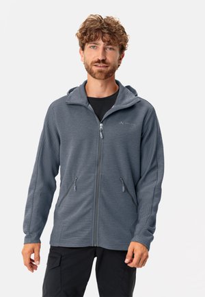 Gray zip-up hoodie made of textured fabric with a hood, front pockets, and contrasting zipper accents, worn over a black shirt.