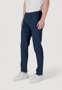 Tamno plave slim-fit hlače napravljene od pamučne mješavine s bočnim džepovima i zatvaranjem na gumb, uparene s bijelim tenisicama.