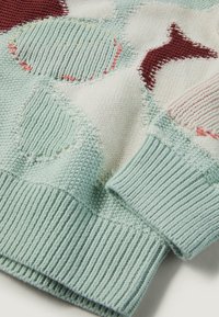 Poignet de pull tricoté avec côtes vert pastel et motif texturé comprenant des formes abstraites crème, vert clair et bordeaux.
