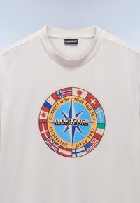 Camiseta de algodón blanca con un gráfico circular que presenta un diseño de brújula y varias banderas, junto con el texto "NAPAPIJRI" mostrado de manera destacada.