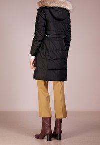 Svart puffjacka med en huva av fuskpäls, horisontellt quiltad design, kombinerad med senapsgula byxor och bourgognefärgade klackstövlar.