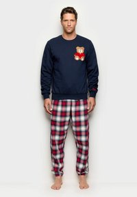 Sudadera azul marino con bordado de oso en el pecho, combinada con pantalones de pijama de franela a cuadros en rojo, blanco y azul marino. Material de algodón, ajuste holgado.