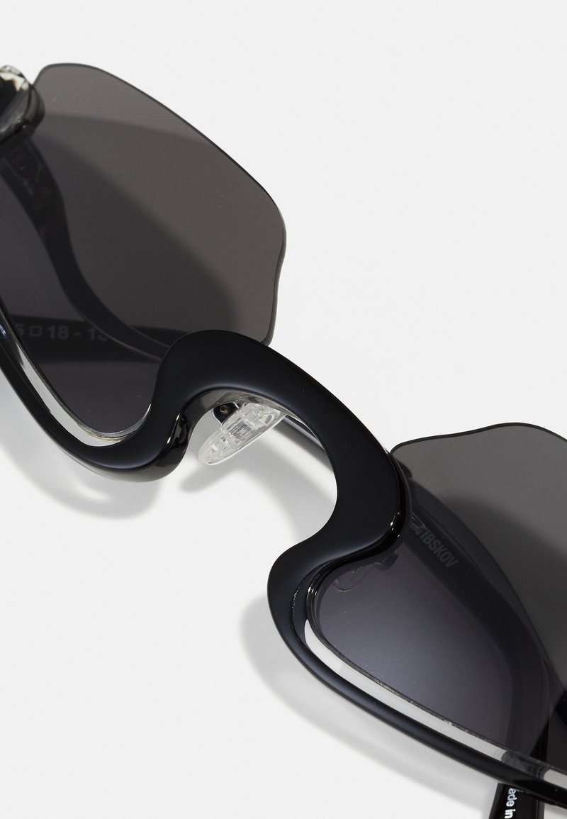 Occhiali da sole neri con lenti curve e sovradimensionate e una montatura liscia e lucida. Presentano naselli trasparenti per un comfort ottimale e un design minimalista.