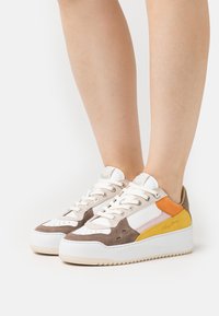 Sneakers med en blandning av beige, brunt, vitt och orange material; klassisk snörningsdesign; texturerad mocka och släta ytor; upphöjd sål.