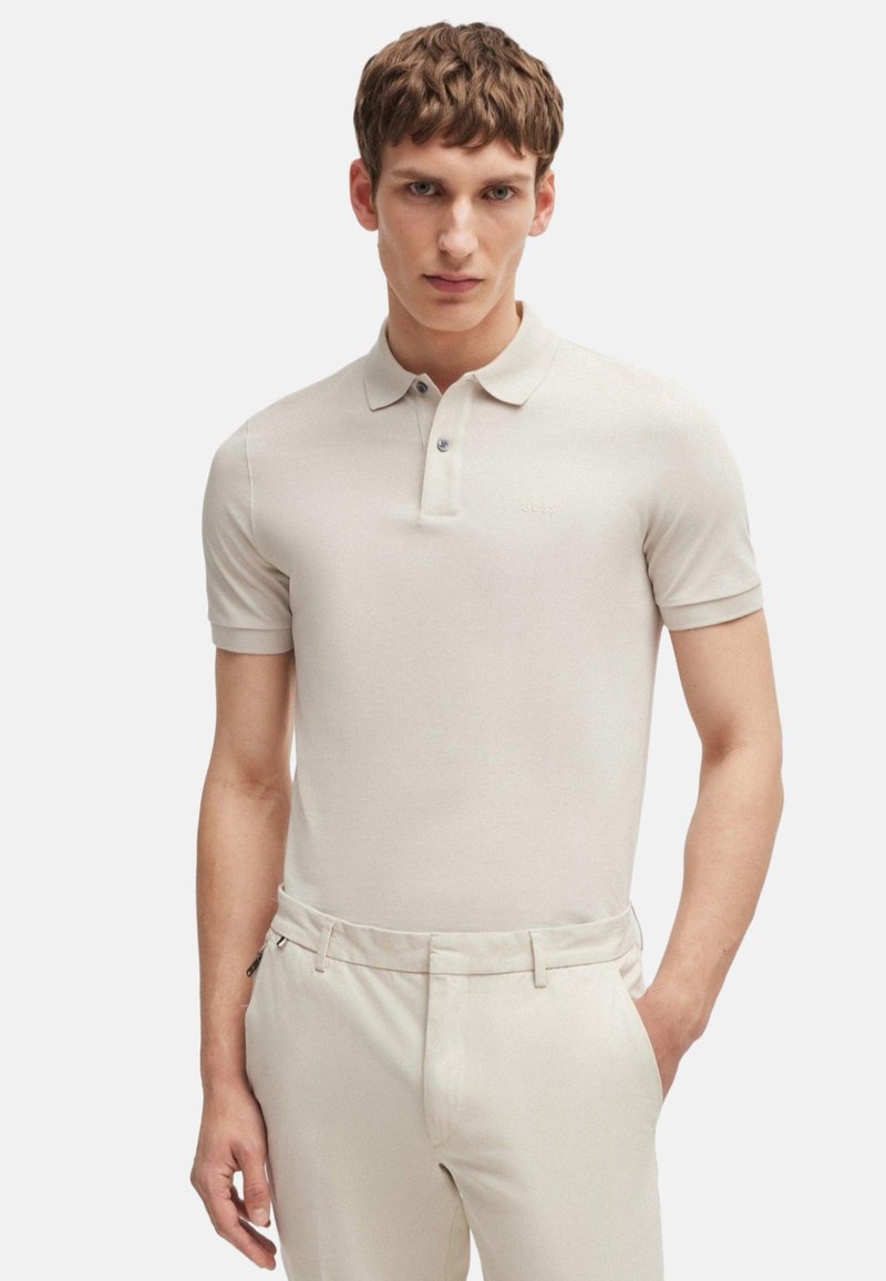 Polo beige à manches courtes en tissu lisse, avec un col et une patte de boutonnage à trois boutons, associé à un pantalon taillé de couleur claire.