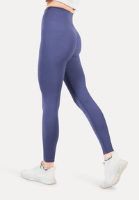 Leggings de tiro alto en un material azul oscuro sólido con una textura suave, presentando un diseño ajustado y acentuados con zapatos deportivos blancos.