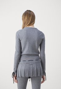 Szary dzianinowy sweter z dopasowanym korpusem i plisowanym tyłem, z prążkowanymi mankietami oraz sznurkami na końcach rękawów, ozdobiony liniami i akcentami.