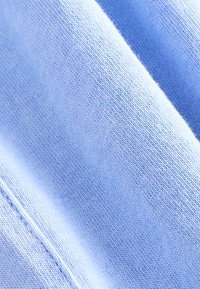 Primo piano di tessuto lavorato a maglia azzurro chiaro che mostra una texture fine e morbida e cuciture dettagliate lungo una cucitura.