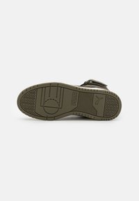 Black shoe with a textured, olive green rubber sole featuring a patterned tread and a prominent logo. Adjustable straps on the upper.
